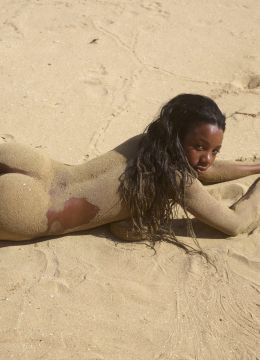 Голая черная девка в песке сжимает большие сиськи руками
